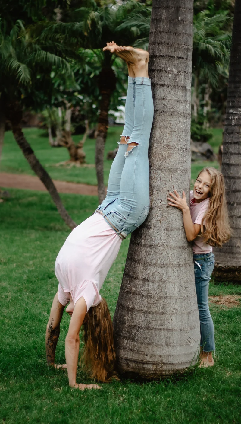 Fun mother daughter posing by palm trunk in tropical Tenerife garden for family portrait session