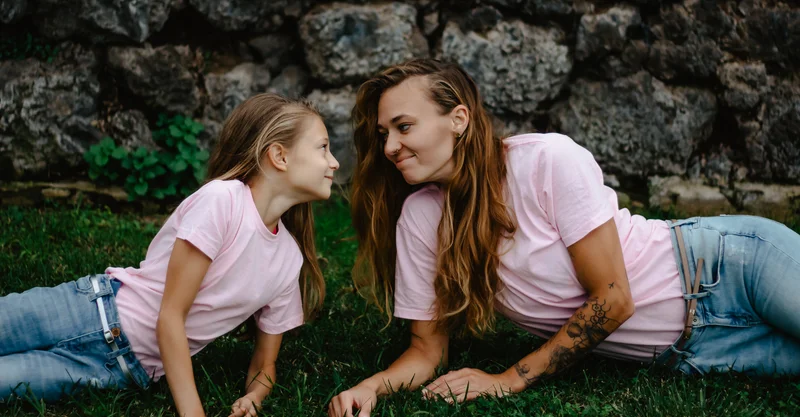 Mother and daughter lying on grass looking at each other in pink shirts Tenerife portrait session