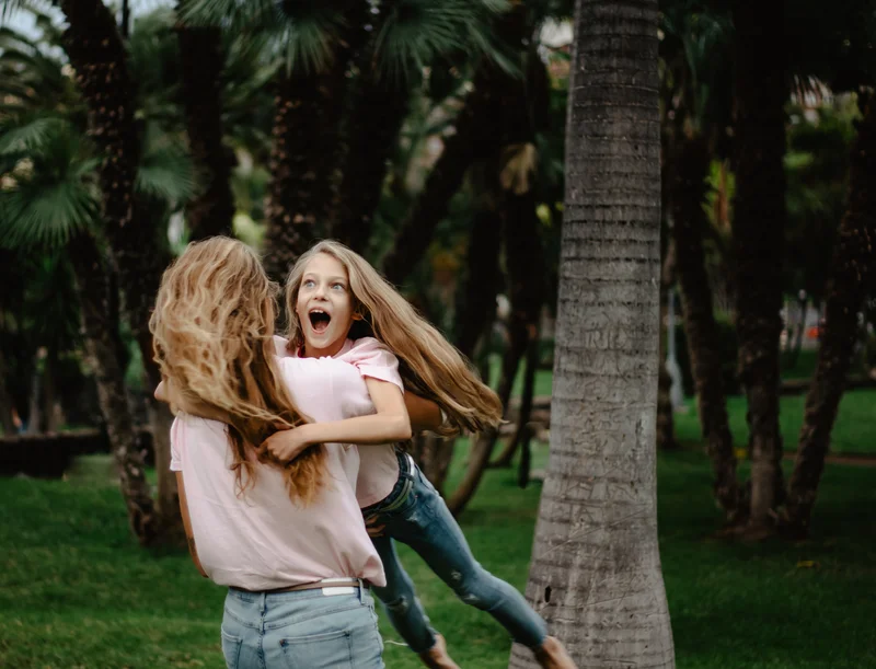 Joyful mother daughter play among palm trees in tropical Tenerife park during lifestyle photography session