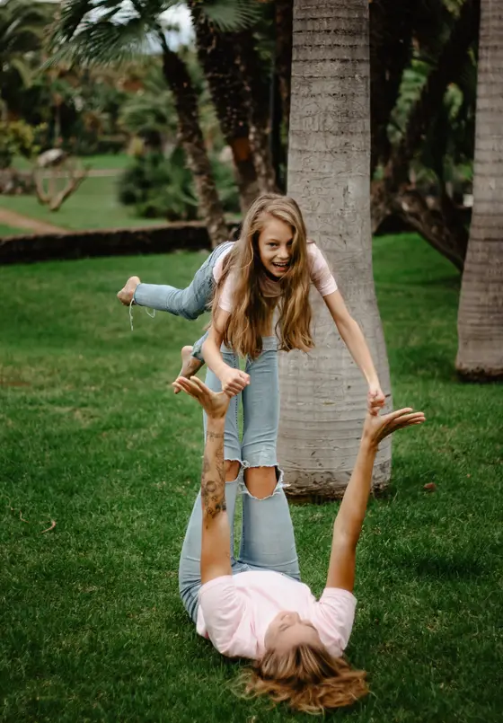 Acrobatic mother daughter play by palm tree in green Tenerife park during family photography session