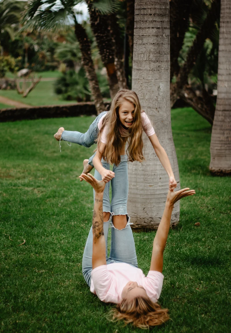Acrobatic mother daughter play by palm tree in green Tenerife park during family photography session