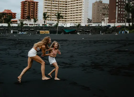 Mother and daughter running playfully on black volcanic beach in Tenerife wearing beach outfits