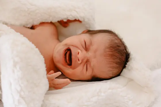 Newborn baby crying on white blanket during natural newborn photography Tenerife session
