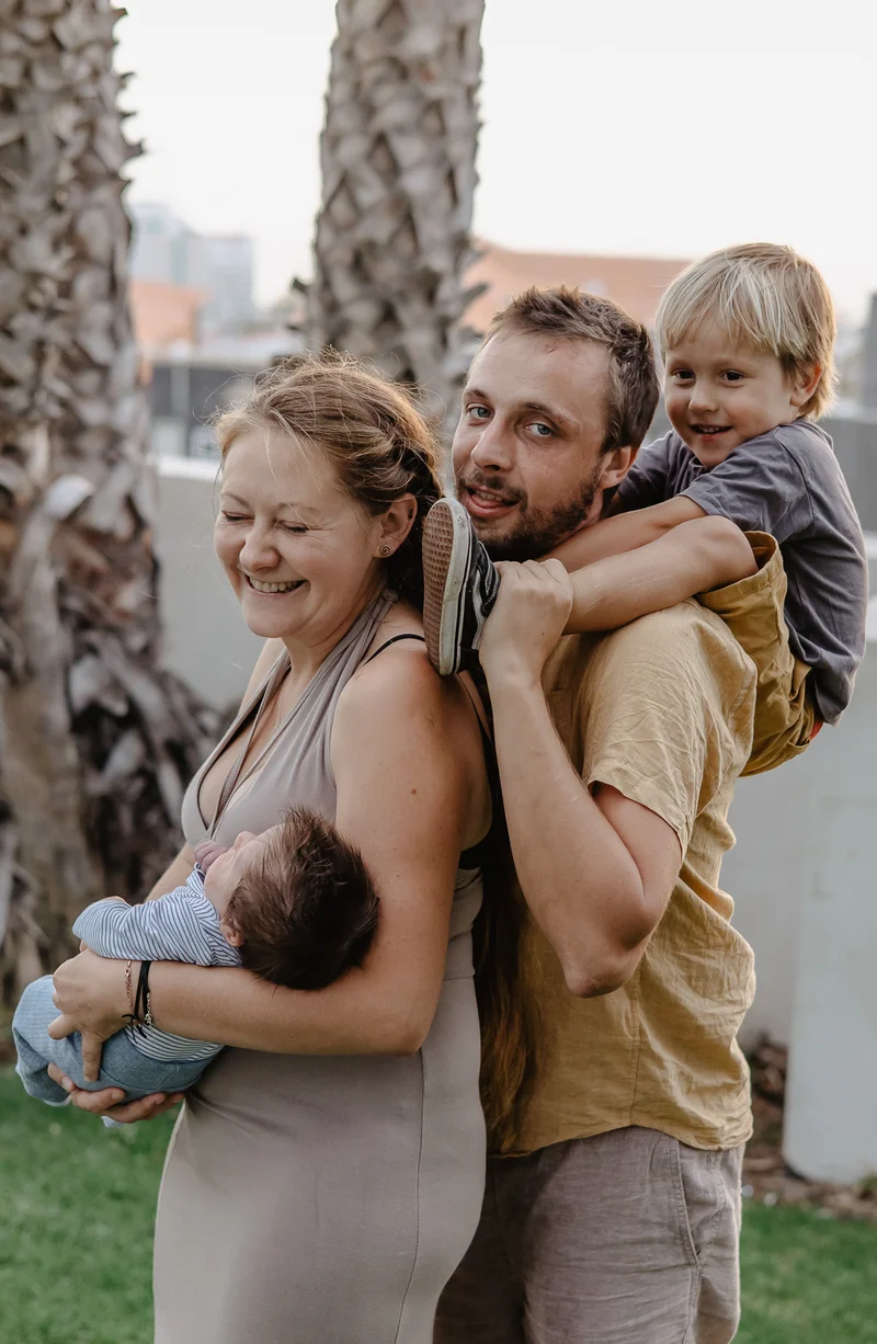 Happy family with newborn and older child among palm trees during newborn photography session Tenerife