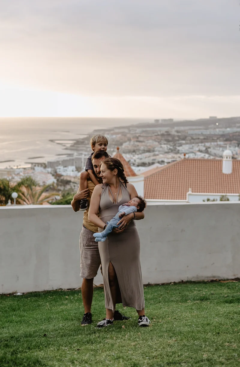 Family with newborn against city view backdrop during outdoor newborn photography session Tenerife
