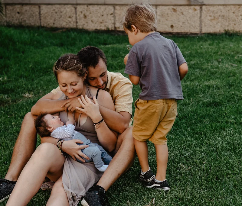 Mother nursing newborn on grass with family during outdoor newborn photography session Tenerife