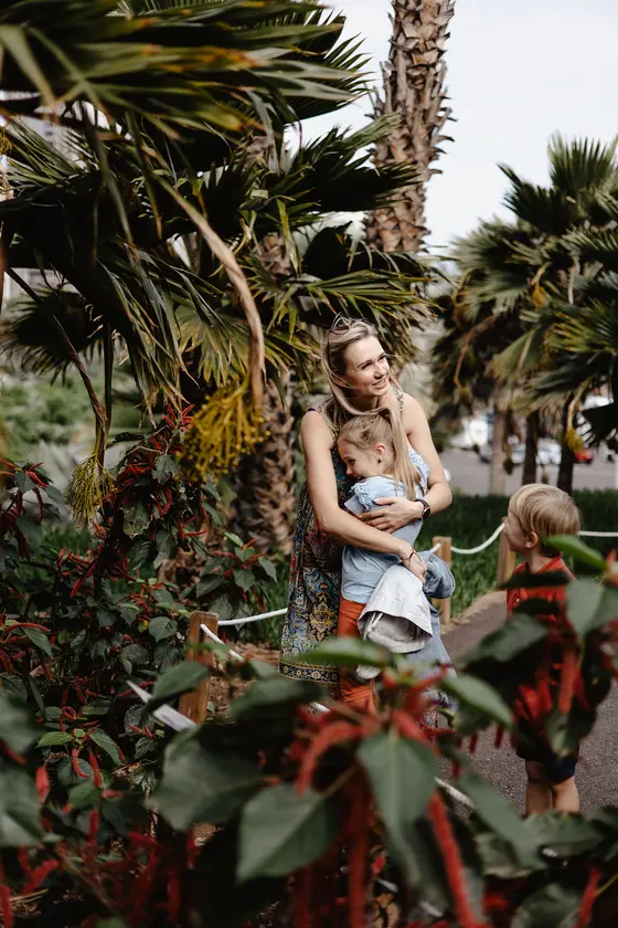 Madre jugando con niños entre palmeras tropicales y plantas coloridas en el Palmetum