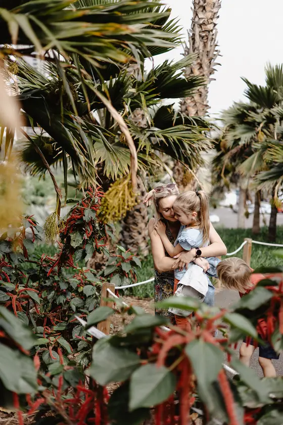 Madre jugando con niños entre palmeras y vegetación tropical en el Palmetum