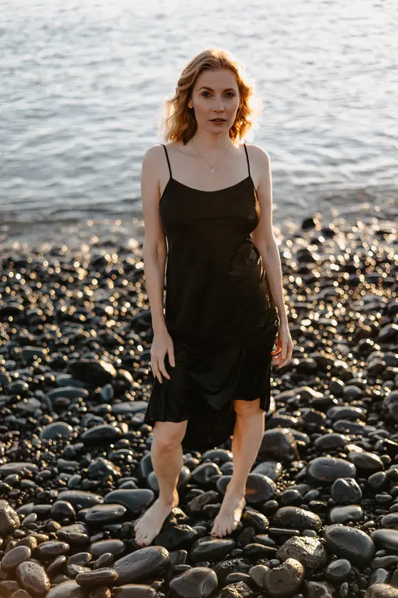 Elegant blonde woman in black dress on rocky Tenerife beach during golden hour light