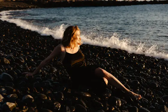 Serene woman sitting on pebbled beach with ocean waves backdrop in Tenerife golden light