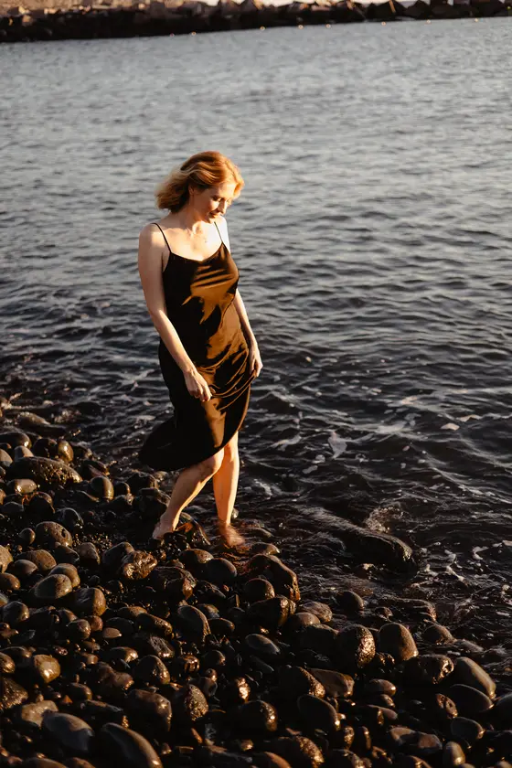 Graceful woman walking on pebbled beach in evening sunset light on Tenerife volcanic coast