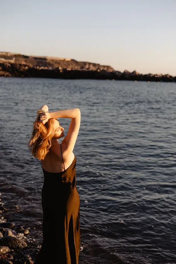 Woman with hands in hair posing on Tenerife coastline with cliff views in golden sunset background