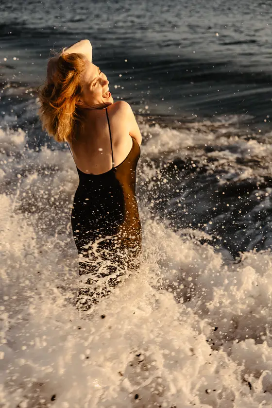 Dynamic woman in black dress enjoying ocean waves on rocky Tenerife beach during sunset