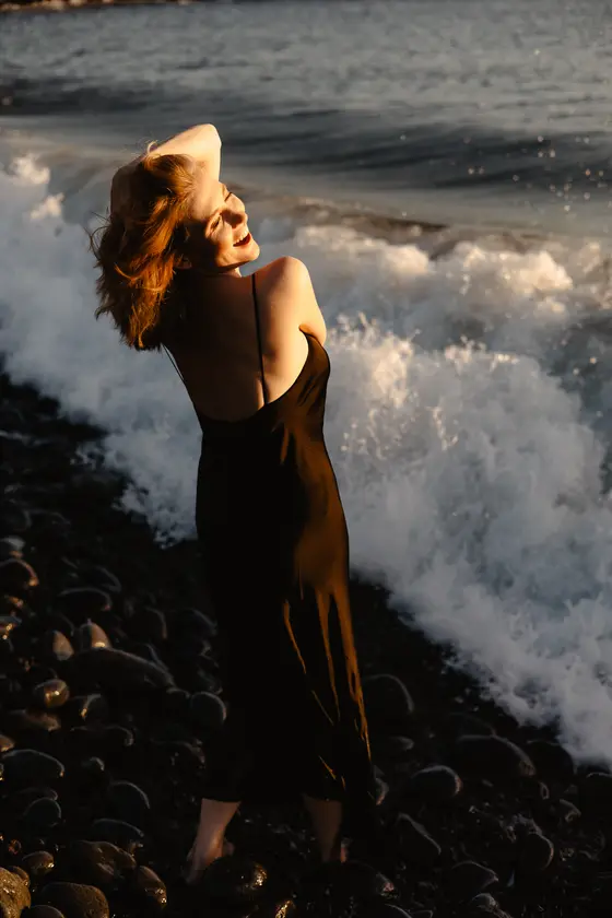 Ecstatic woman with arms raised enjoying ocean waves during golden hour on Tenerife beach