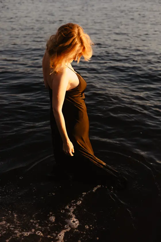 Delicate woman in profile standing knee-deep in ocean during golden hour on Tenerife coast