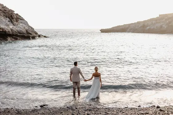 Wedding couple holding hands standing by ocean in golden sunset light