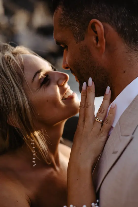 Close-up of tender face touch between wedding couple in golden sunlight during photo session