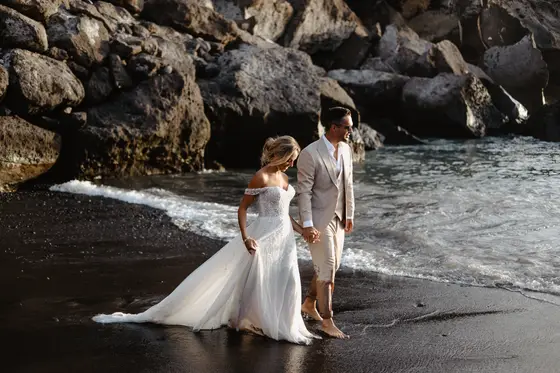 Wedding couple walking on black volcanic beach against rocky coastline at Playa Paraiso