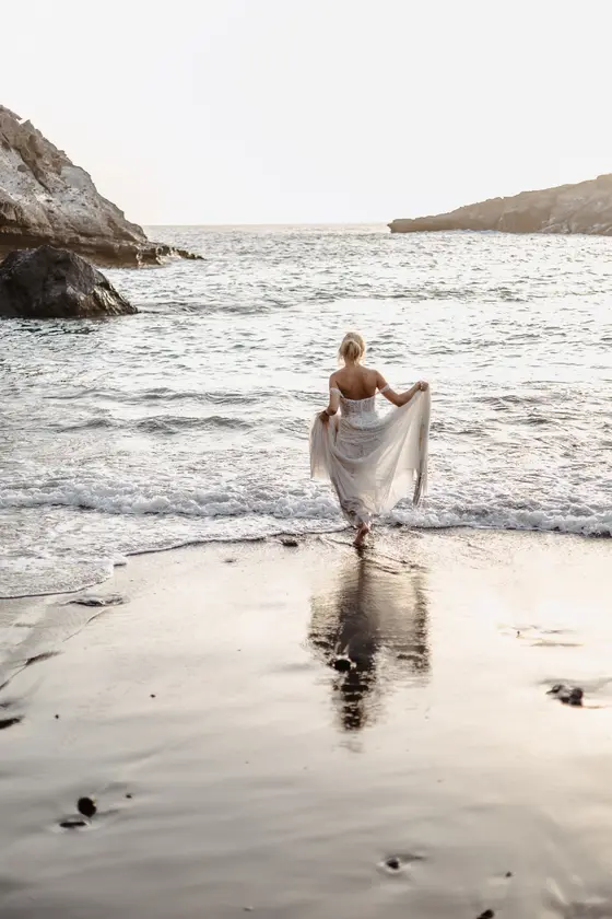 Bride in white dress holding train while standing in ocean waves at Playa Paraiso beach
