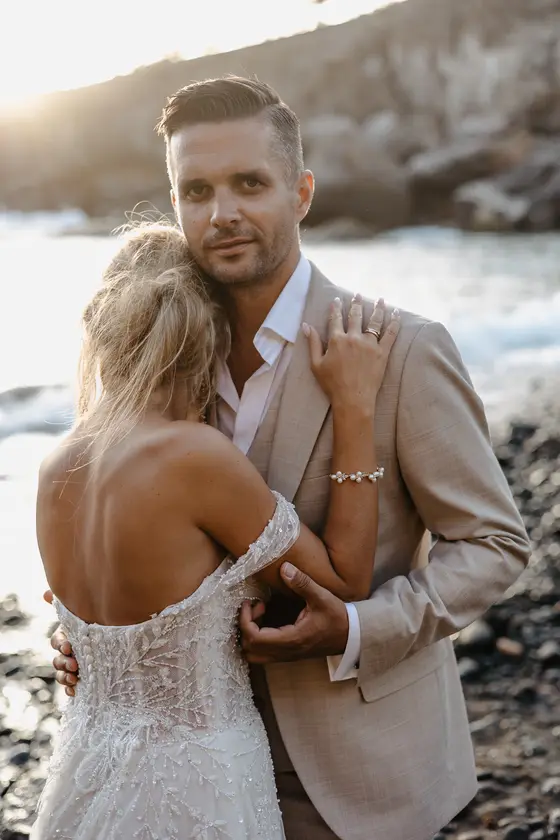 Bride nestled in groom's arms against black volcanic beach backdrop in Tenerife
