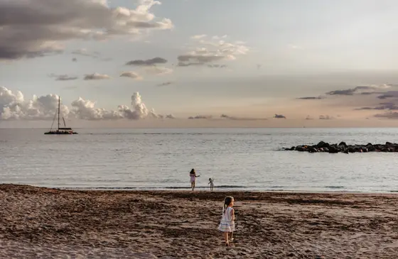 Children playing on beach with sailboats in background during family session in Tenerife