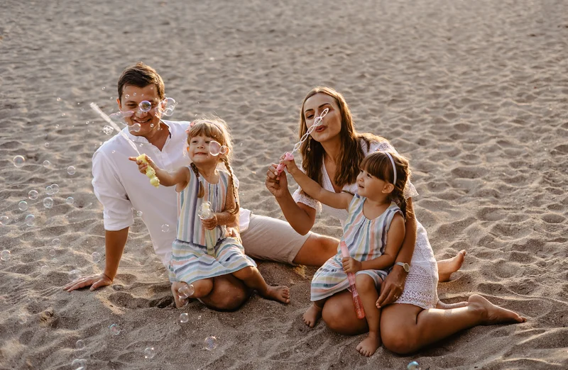 Family of four making soap bubbles on sand during beach photo session