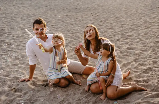 Family of four making soap bubbles on sand during beach photo session