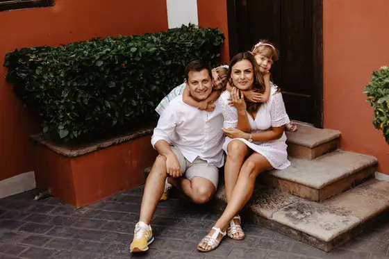 Family sitting on stone steps of Spanish villa wearing white summer clothes