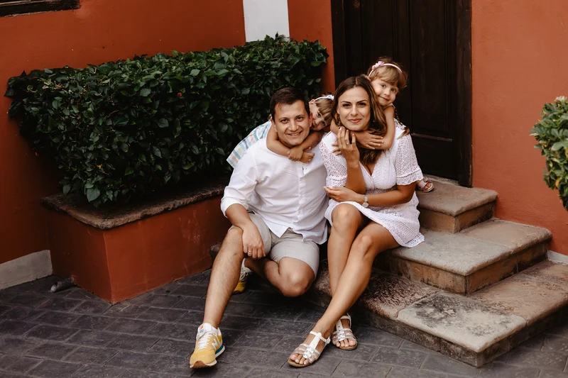 Family sitting on stone steps of Spanish villa wearing white summer clothes