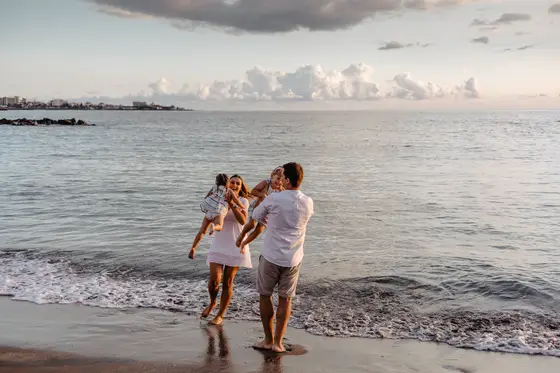 Father lifting young child into air on beach during sunset wearing white clothing