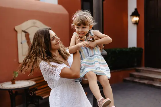 Mother lifting little girl against Spanish villa backdrop with terracotta walls and columns