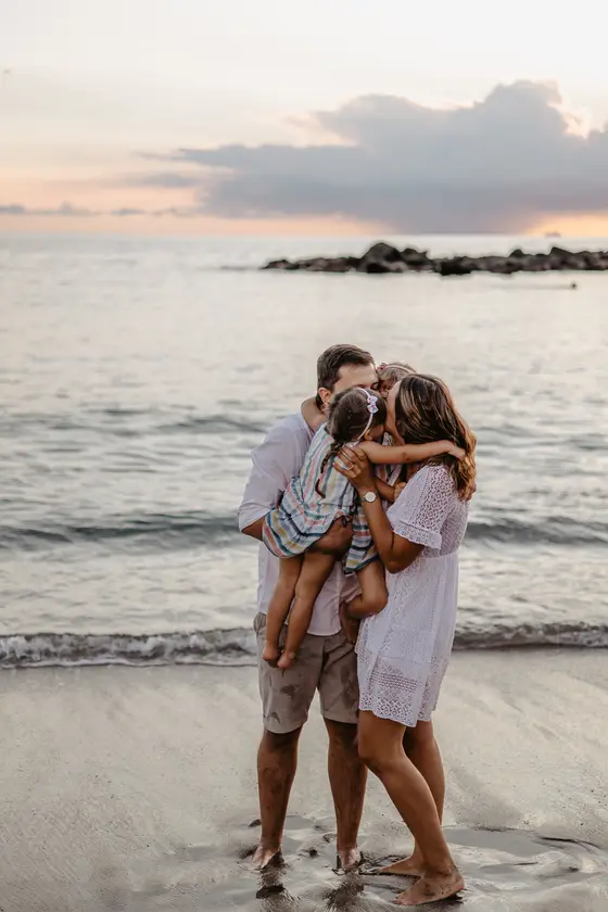 Parents embracing children on beach during sunset with ocean and clouds in background