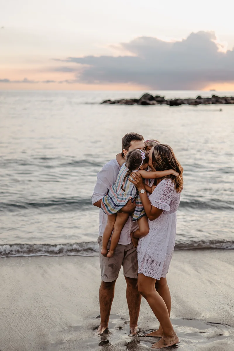 Parents embracing children on beach during sunset with ocean and clouds in background