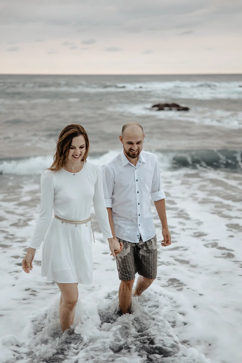 Szczęśliwa para spaceruje w falach oceanu na czarnej plaży Teneryfa