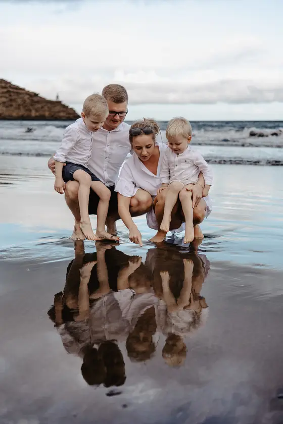 Tenerife family session with parents and children playing in water on volcanic beach