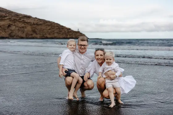 Happy family sitting on wet Tenerife volcanic beach with ocean waves in background
