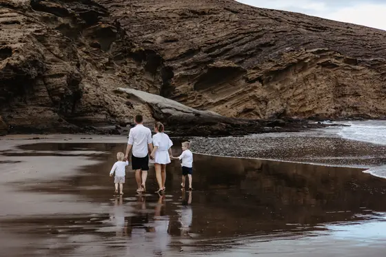 Family photography Tenerife on volcanic beach with four children walking along ocean shore
