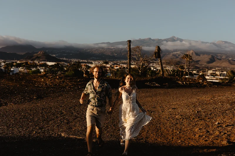 Pareja enamorada corriendo en terreno volcánico de Tenerife con montañas de fondo