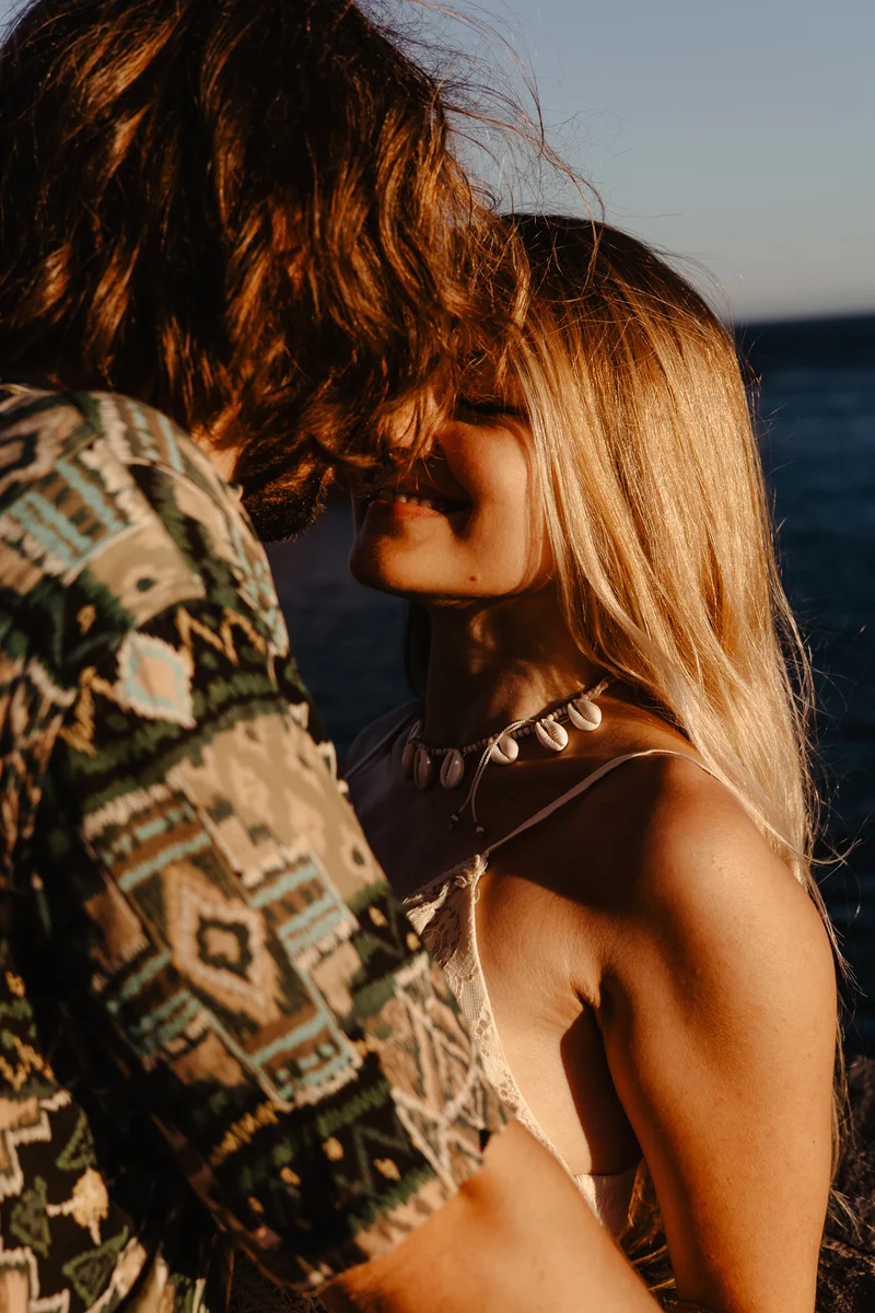 Retrato íntimo de pareja con cabello flotante contra océano Atlántico y cielo fondo