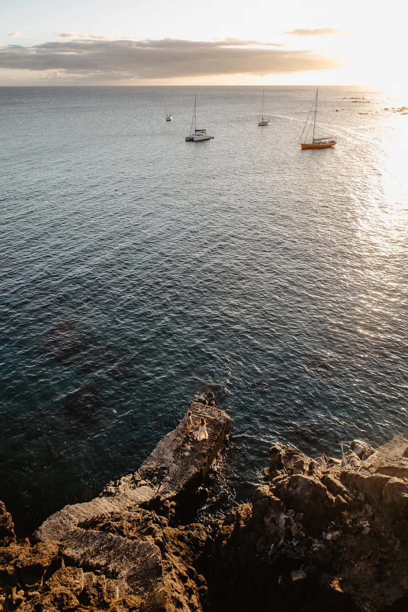 Atardecer sobre océano con yates visto desde rocas volcánicas de Tenerife
