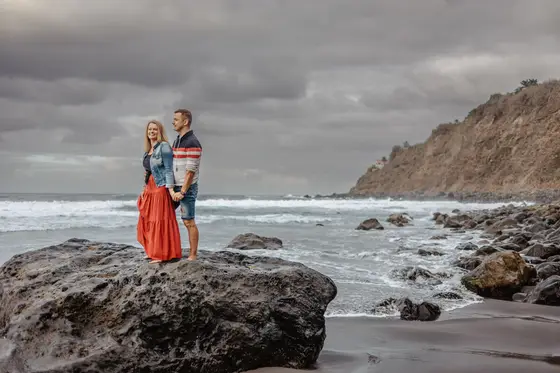 Retrato romántico de pareja en rocas volcánicas playa Socorro Tenerife durante sesión fotografía familiar lifestyle