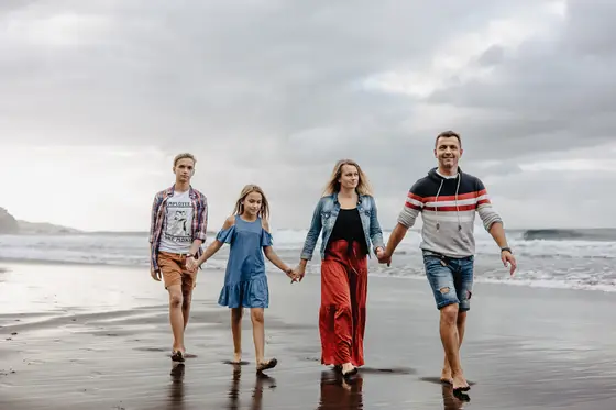 Familia feliz tomados de la mano caminando en arena húmeda playa Socorro durante sesión fotografía familiar Tenerife