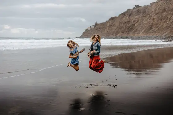 Madre e hija saltando alegremente en el aire playa Socorro durante sesión fotografía familiar juguetona Tenerife