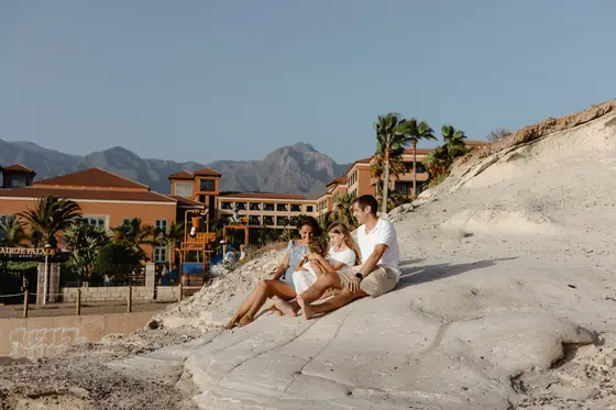 Family with children in white outfits against South Tenerife hotels and mountains during golden hour