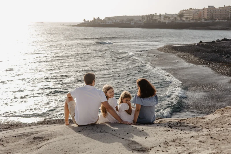 Family sitting by ocean during sunset on South Tenerife beach with waves in background