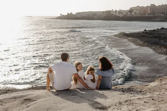 Family sitting by ocean during sunset on South Tenerife beach with waves in background