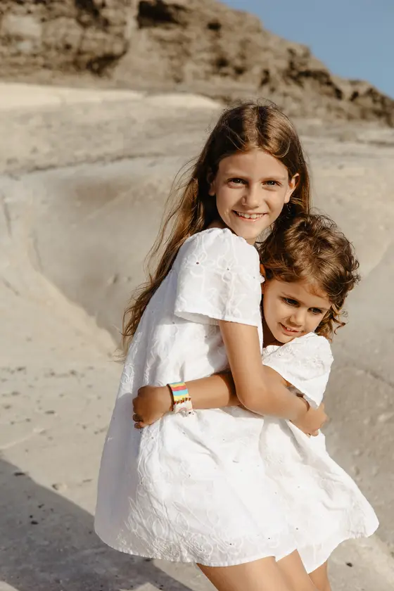 Sisters in white dresses embracing on bright volcanic cliffs of South Tenerife