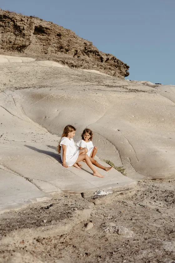 Sisters in white clothing relaxing on smooth volcanic surfaces of South Tenerife