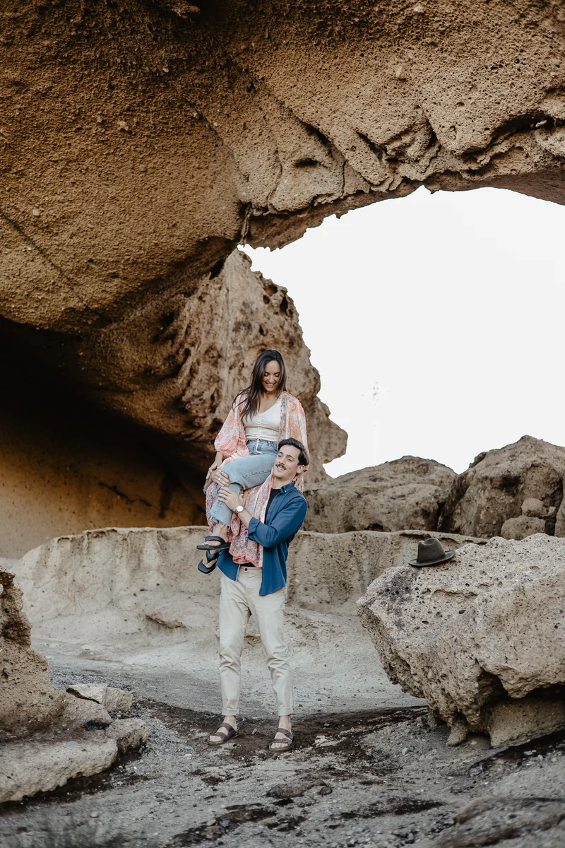 Couple in colorful outfits posing in shadow of monumental Tenerife rock arch