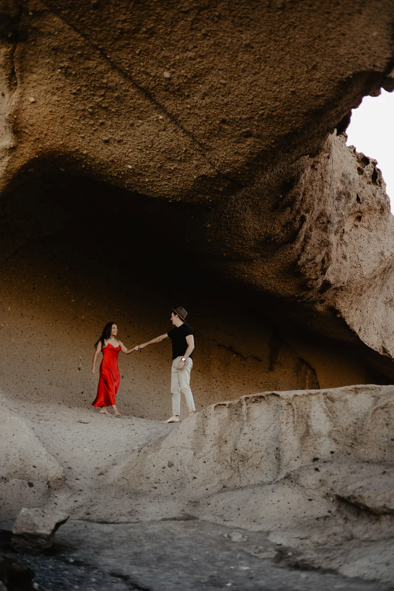 Couple dancing in red dress under natural vault of rock arch in Tenerife
